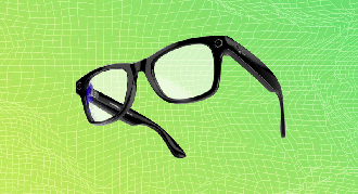 A pair of black smart glasses with built-in cameras and sensors, floating against a green and yellow gradient grid background.