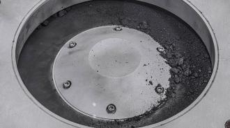 A close up of a metal container with bits of the Bennu asteroid sample on it