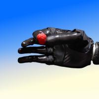 A black robotic hand holding a small red object against a blue and beige gradient background.