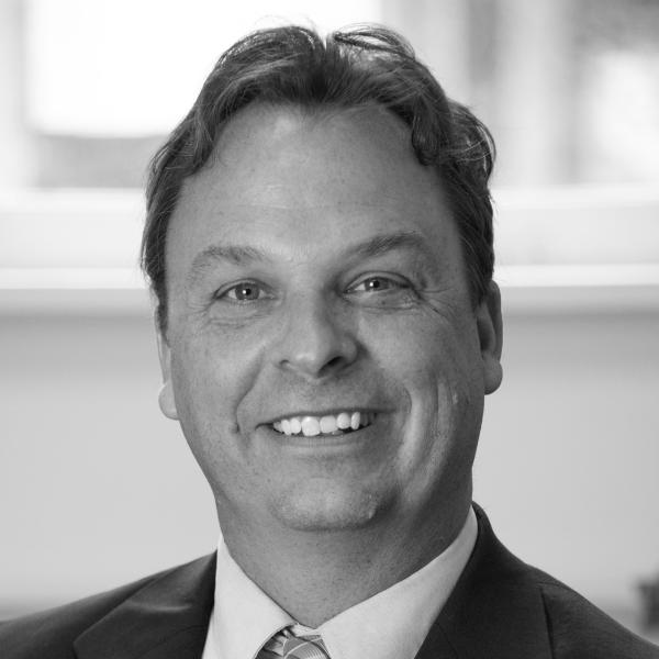 A man in a suit and tie smiling, photographed indoors in black and white.