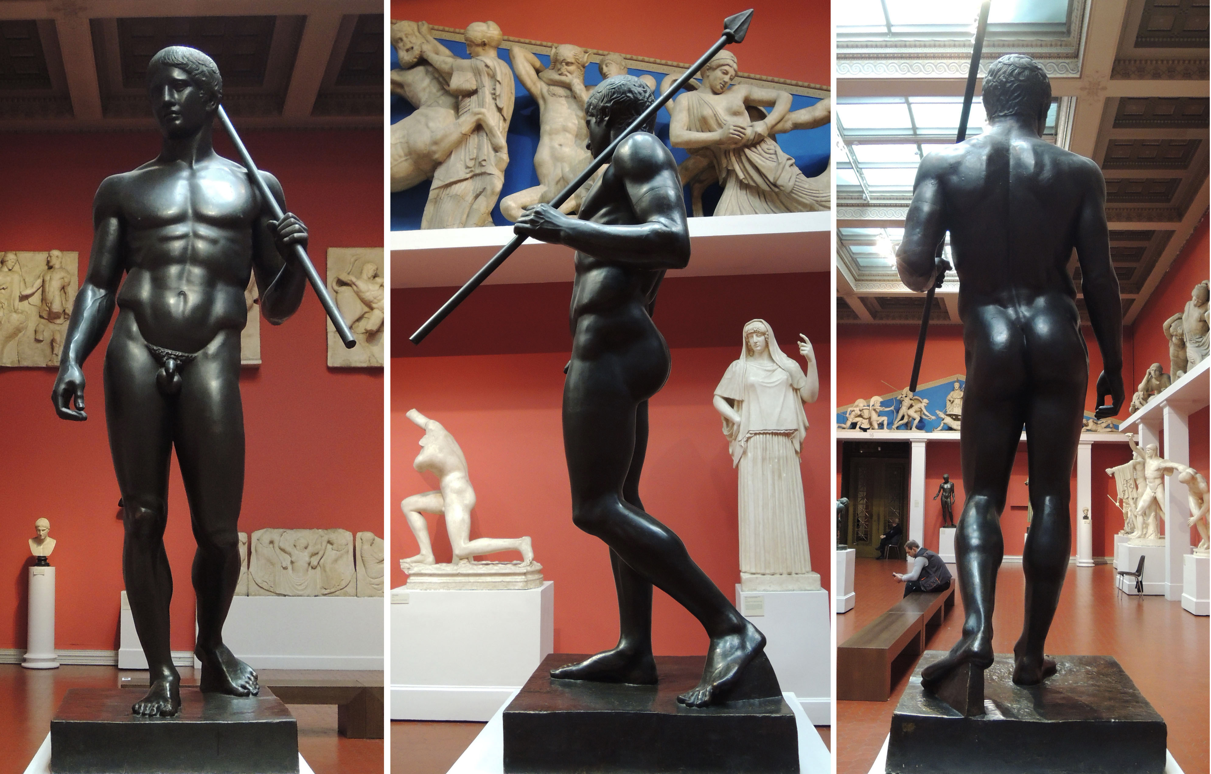 Three views of a black statue of a nude male holding a spear, displayed in a museum gallery with classical sculptures and red walls in the background.