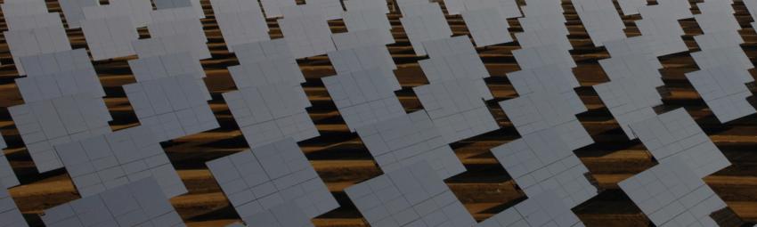 Aerial view of multiple large, square solar panels positioned at an angle on a solar farm.