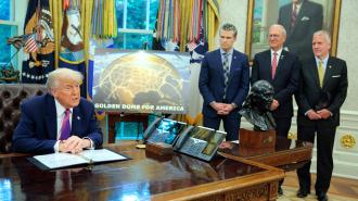 Former President Donald Trump sits at the Oval Office desk with paperwork while three men stand nearby next to a bust and a “Golden Dome for America” sign.