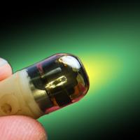 A close-up of a person's fingers holding a small, transparent electronic component with a green background.