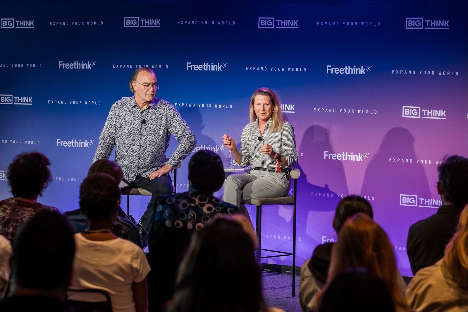 Two speakers sit on stage in front of a seated audience, engaging in a discussion at a Freethink and Big Think event.