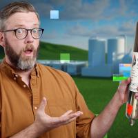A man with glasses and a beard holds a cylindrical object labeled "Transport Document" outside in front of an industrial backdrop.
