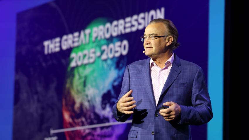 A man in a blue suit gives a presentation titled "The Great Progression 2025-2050" with a colorful graphic background.