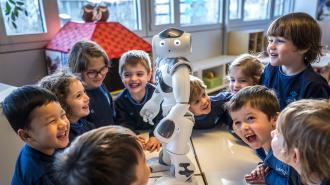 A group of young children in a classroom gather around a small humanoid robot, smiling and laughing.