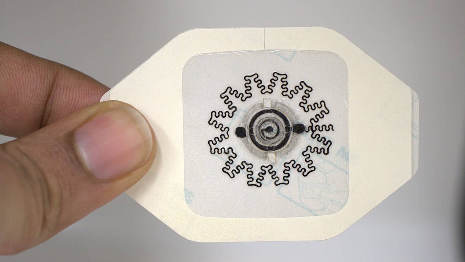 A hand holds a soft, flexible wearable device with a snowflake-like design on a white backing.