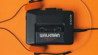 A black Sony Walkman cassette player with orange foam headphones is displayed on an orange background.