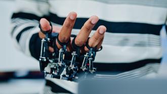 A person wearing a mechanical exoskeleton device on their hand, with metal components attached to each finger.