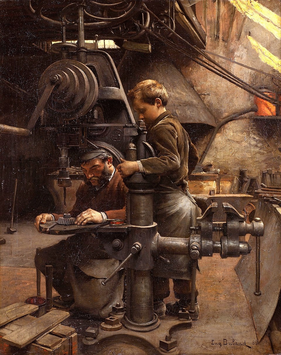 A man operates a large industrial machine while a young boy stands beside him, assisting in a workshop filled with tools and machinery.