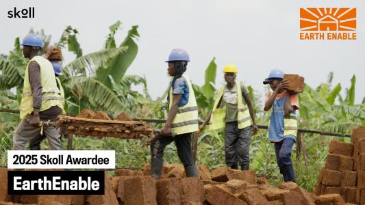 Five workers wearing safety gear and helmets carry and stack bricks outdoors, with green plants and the EarthEnable logo visible in the background. Text indicates "2025 Skoll Awardee EarthEnable.