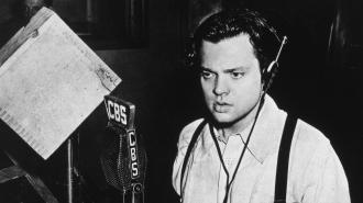 A man wearing headphones speaks into a CBS microphone in a radio studio, with audio equipment visible in the background.