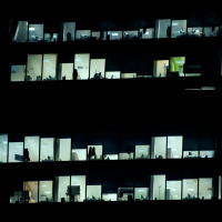 Three floors of a dimly lit office building with illuminated windows showing desks, computers, and office equipment.