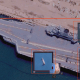 Satellite view of an aircraft carrier docked at a port, with inset images showing maps, close-ups, and a highlighted red area.