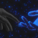A human hand reaches toward a glowing, blue holographic deadbot hand against a dark background with scattered points of light.
